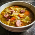 Close-up of a bowl of delicious Cabbage and Kielbasa Soup with carrots and sausage.