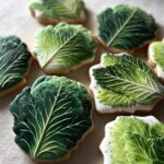 Close-up of several Cabbage-Shaped Sugar Cut-Outs, decorated with green icing and white details.