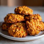 A stack of freshly baked Carrot Cake Oatmeal Cookies on a white plate, showing visible carrots and oats.