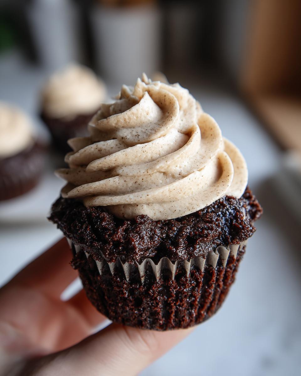 Close-up of a Chocolate Guinness Cupcake with creamy frosting, held in a hand.