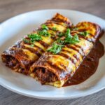 Two Chocolate Mole Enchiladas on a white plate, topped with cheese and herbs. A perfect Romantic Dinner.