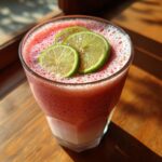 Glass of Coconut Strawberry Soup with Lime, garnished with lime slices, on a wooden surface.