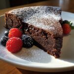 A slice of Flourless Chocolate Valentine Torte dusted with powdered sugar, garnished with fresh berries.