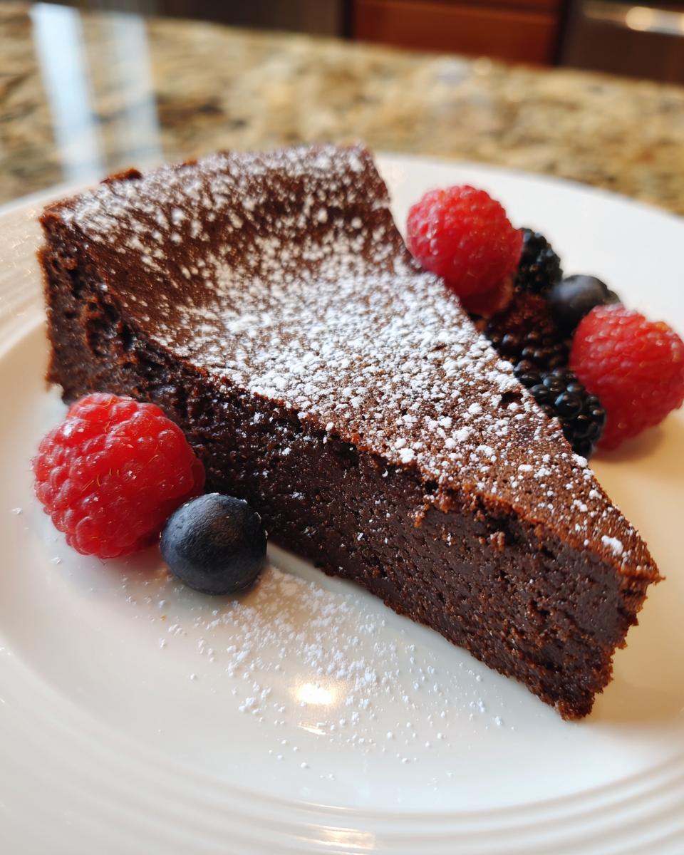 A slice of Flourless Chocolate Valentine Torte dusted with powdered sugar and garnished with fresh berries.