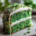 A slice of green Four-Leaf Clover Sugar Cookie Cake with white frosting and sprinkles.