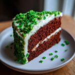 A slice of Green Velvet Cake with Shamrock Sprinkles on a white plate, close-up.