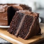 Close-up of a slice of Guinness Chocolate Layer Cake on a wooden board, showing the moist cake layers.