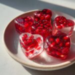 Close-up of heart-shaped pomegranate ice cubes on a white plate, perfect for a refreshing drink. The image highlights the Heart‑Shaped Pomegranate Ice Cubes.