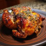 A whole, roasted Lemon Herb Roasted Chicken on a plate, garnished with herbs.