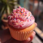 Close-up of a Quick Pink Velvet Cupcake with pink frosting and colorful sprinkles.
