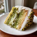 A delicious slice of Pistachio Surprise Cake on a white plate, showcasing layers and pistachio.