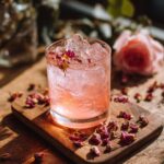Close-up of a Rose Petal Gin and Tonic cocktail garnished with rose petals on a wooden board.