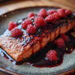Close-up of seared salmon topped with fresh raspberries and a raspberry balsamic glaze.