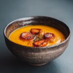 Close-up of a bowl of Sweet Potato and Carrot Ginger Soup with garnish.