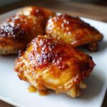 Close-up of air fryer apricot glazed chicken thighs on a white plate, showcasing the delicious glaze.