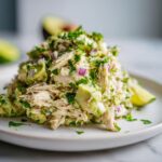 Close-up of a serving of Avocado Chicken Salad with avocado chunks, red onion, and herbs.
