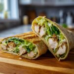 Close-up of a grilled Chicken Caesar Wrap cut in half, showing chicken, lettuce, and Caesar dressing.