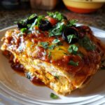 Close-up of a slice of Chicken Stacked Enchiladas with cheese, sauce, olives, and cilantro.