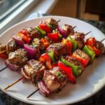 Close-up of delicious Lamb Kabobs with red and green bell peppers and red onion on a white plate.
