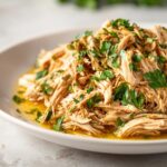 Close-up of shredded Instant Pot Lemon Chicken, garnished with fresh parsley, in a white bowl.