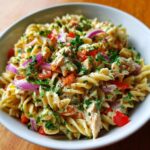 Close-up of a bowl of Lime Chicken Pasta Salad with pasta, chicken, red onion, and herbs.