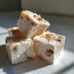 Close-up of four Apple Yogurt Frozen Dog Treat Cubes stacked on a white plate, showing the texture and ingredients.