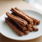 Close-up of a pile of homemade Beef and Brown Rice Dog Treat Sticks on a white plate.