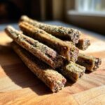 Close-up of a pile of delicious Beef and Green Bean Dog Treat Sticks on a wooden board.