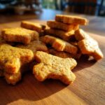 Close-up of a pile of homemade Chicken & Oat Crunchy Dog Crackers on a wooden surface.