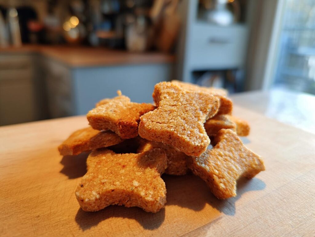 Close-up of a pile of bone-shaped Chicken & Oat Crunchy Dog Crackers on a wooden surface.