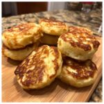 Pile of golden-brown Peanut Butter Banana Dog Pancake Bites on a wooden board.