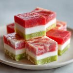 Stack of colorful Watermelon Coconut Frozen Dog Treat Squares on a white plate.